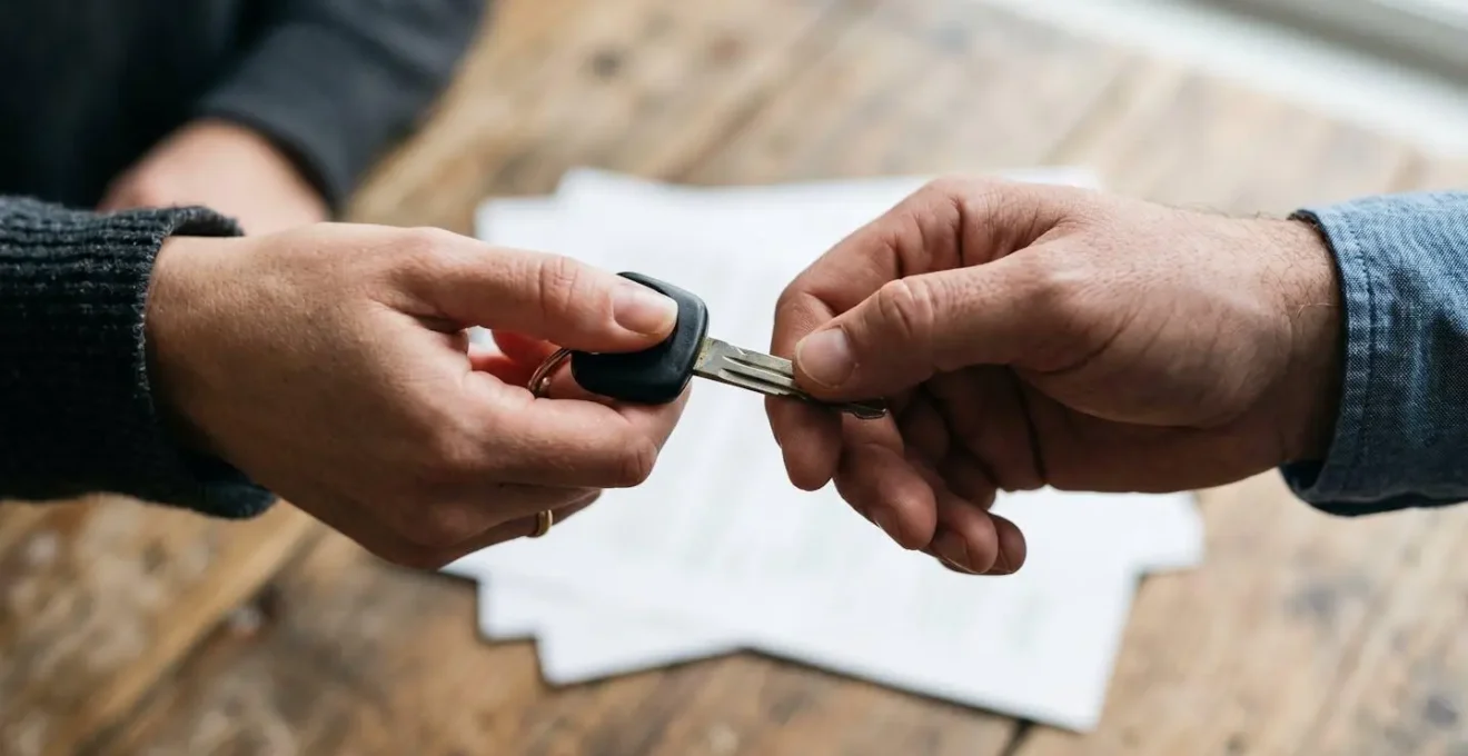 Échange de clés de voiture entre deux personnes, symbolisant la location entre particuliers, avec des documents de contrat en arrière-plan.