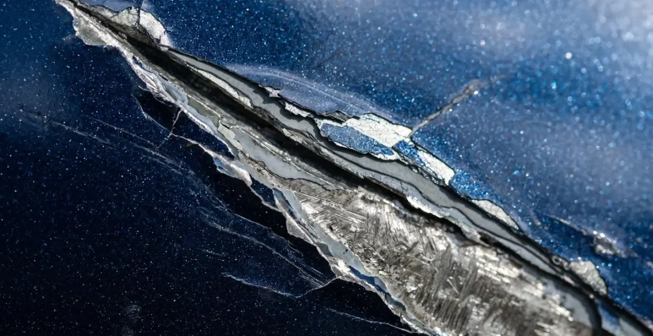 Vue macro d'une rayure profonde sur la carrosserie métallique d'une voiture avec reflets lumineux